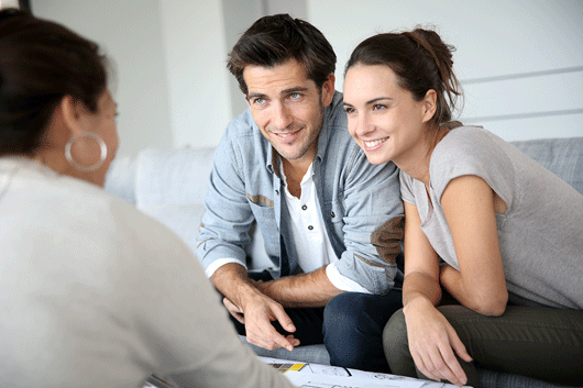 photo of a happy couple sitting on a couch applying for a mortgage with a loan officer woman
