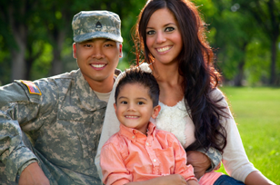 photo of a happy parents with a toddler son in the middle sitting on a lawn and father in veteran uniform
